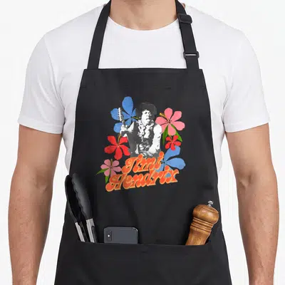 Tablier de cuisine noir avec illustration rétro de Jimi Hendrix entouré de fleurs roses, rouges et bleues et du texte Timi Hendrix orange.