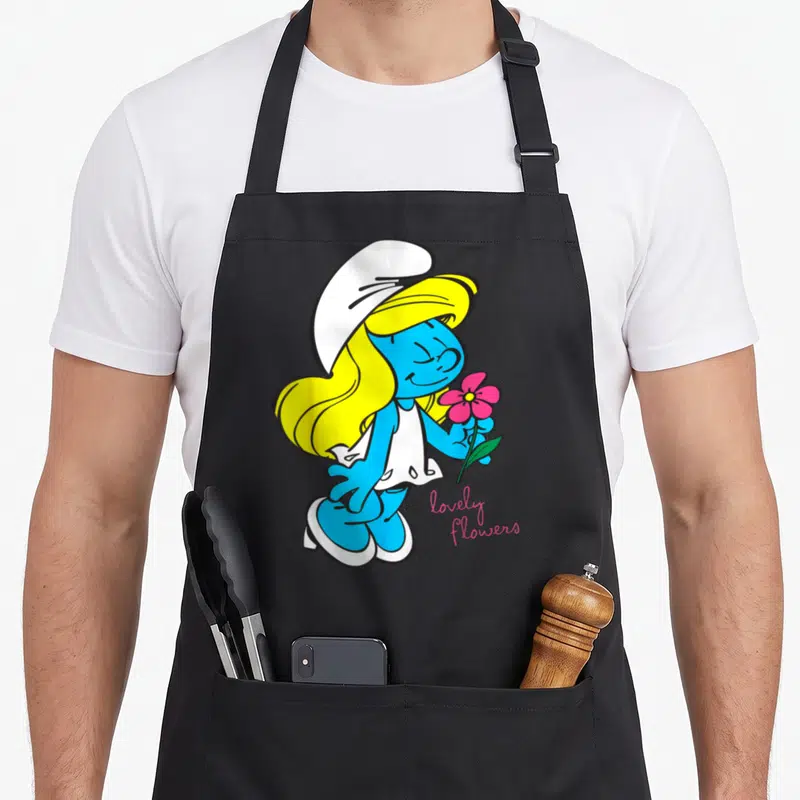 Tablier de cuisine noir avec Smurfette blonde tenant une fleur rose et l'inscription « lovely flowers » en bas à droite.