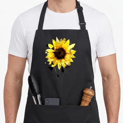 Tablier de cuisine noir avec un tournesol jaune stylisé en polygones géométriques noirs et des tiges fines minimalistes.