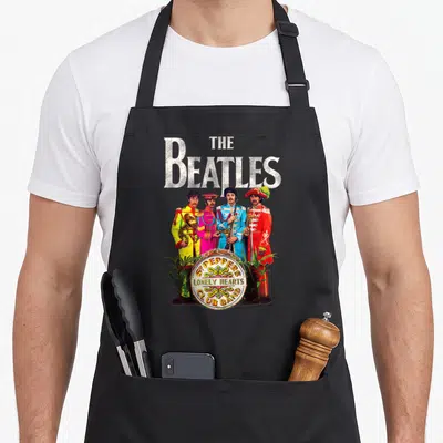 Tablier de cuisine noir avec l'affiche des cœurs solitaires du Sergent Pepper des Beatles en uniforme coloré.
