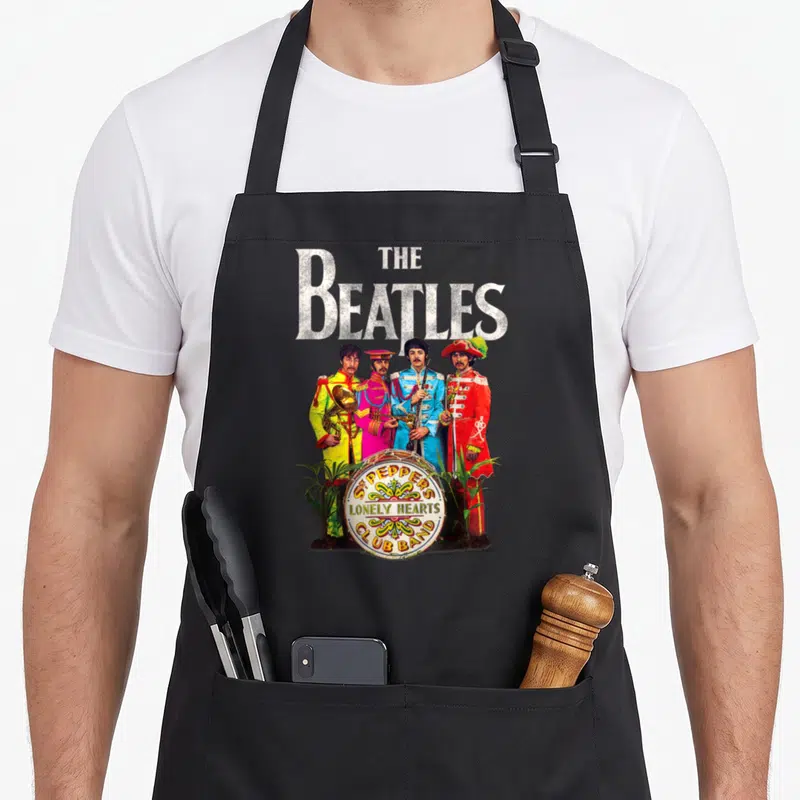 Tablier de cuisine noir avec l'affiche des cœurs solitaires du Sergent Pepper des Beatles en uniforme coloré.