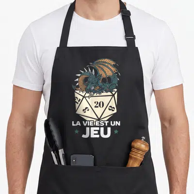 Tablier de cuisine noir avec un D20 beige, un dragon bleu et orange, et le texte La Vie Est Un Jeu en blanc.