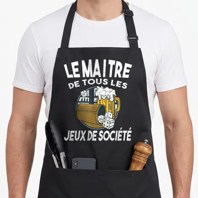 Tablier de cuisine noir avec inscription LE MAITRE DE TOUS LES JEUX DE SOCIÉTÉ et illustration de gobelet à bière avec des dés.