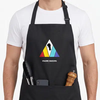 Tablier de cuisine noir avec un grand triangle coloré et une silhouette noire au centre, surmontant le texte Imagine Dragons Evolve.