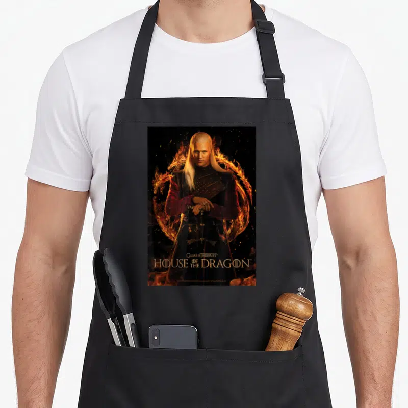Tablier de cuisine noir avec un personnage aux cheveux blonds entouré de flammes et le titre House of the Dragon en bas.
