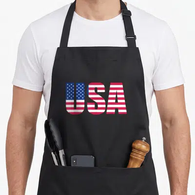 Tablier de cuisine noir avec l'inscription USA stylisée aux couleurs et motifs du drapeau américain.