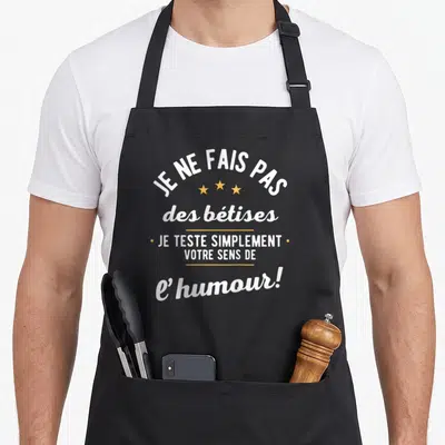 Tablier de cuisine noir avec le texte blanc Je ne fais pas des bêtises et trois étoiles jaunes au centre du dos.