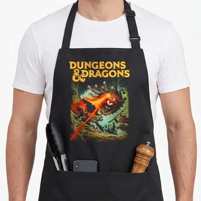 Tablier de cuisine noir avec une illustration colorée d'un béhérot tirant un rayon laser sur des personnages en armure.