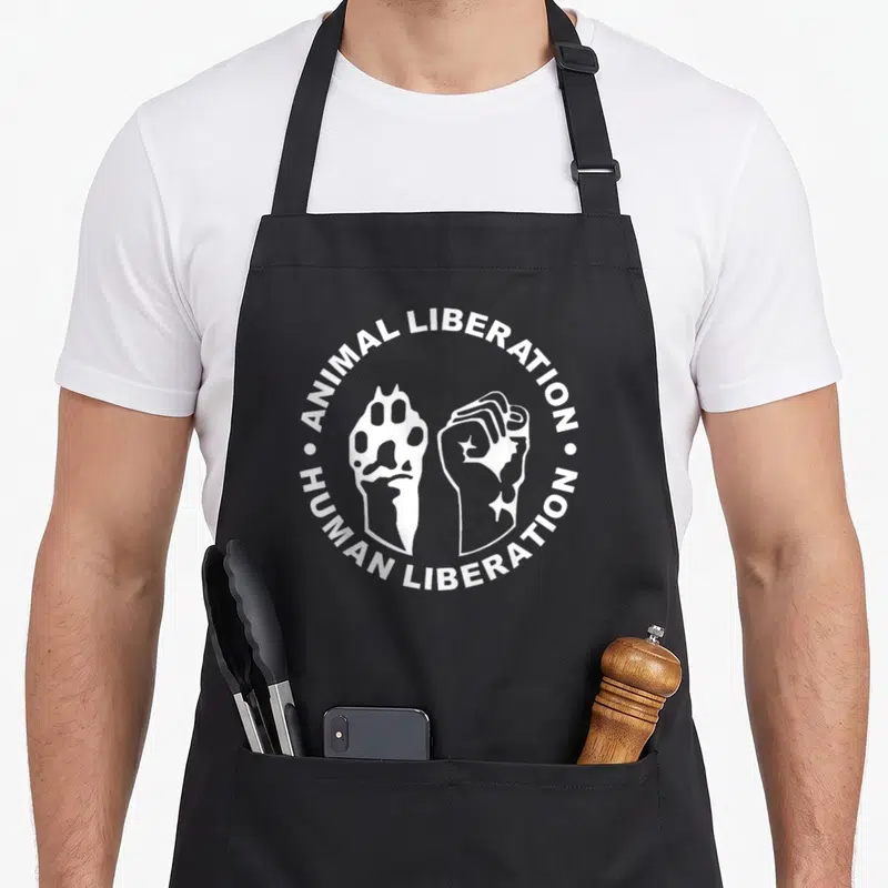 Tablier de cuisine noir avec un logo circulaire blanc montrant une patte d'animal et un poing humain serré.