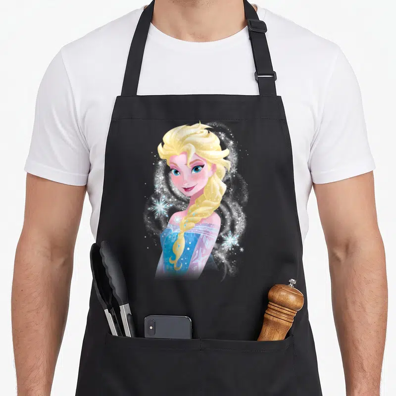 Tablier de cuisine noir avec illustration colorée d'Elsa aux cheveux blonds et flocons de neige scintillants autour d'elle.