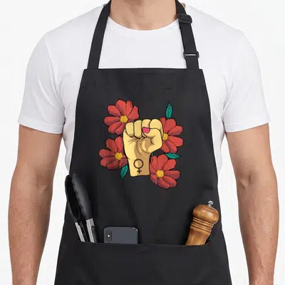 Tablier de cuisine noir avec un poing levé entouré de fleurs rouges et le symbole féminin sur le poignet.