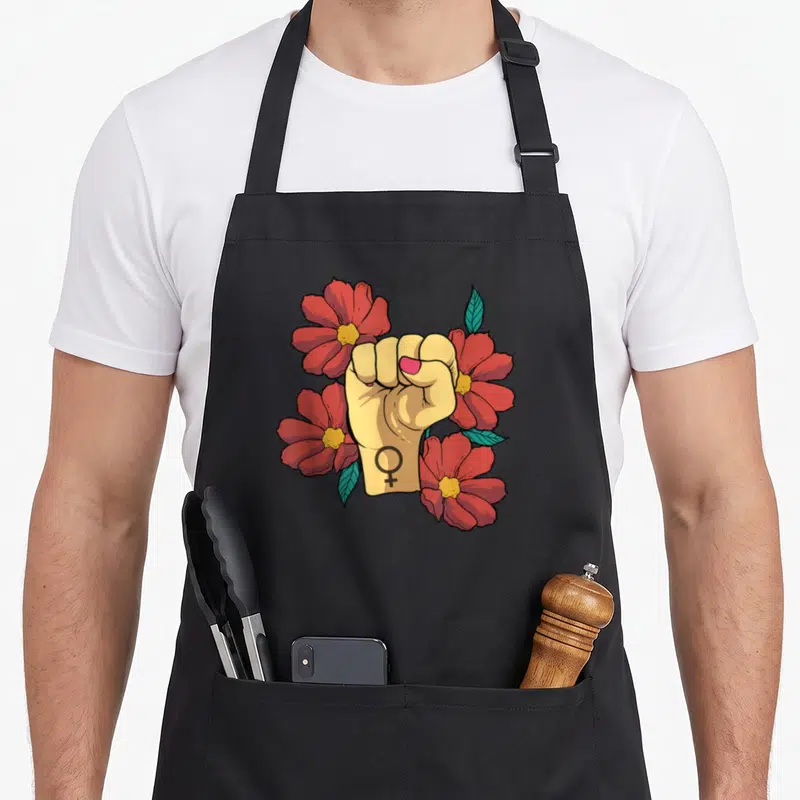 Tablier de cuisine noir avec un poing levé entouré de fleurs rouges et le symbole féminin sur le poignet.