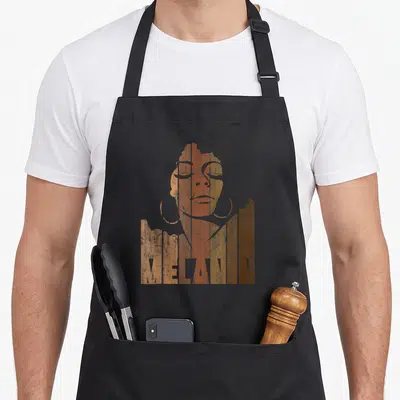 Tablier de cuisine noir avec portrait stylisé aux teintes ocre et le mot Melanin en typographie verticale déstructurée.