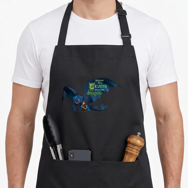 Tablier de cuisine noir avec Toothless, Hiccup et le titre How to Train Your Dragon imprimé en vert et blanc.