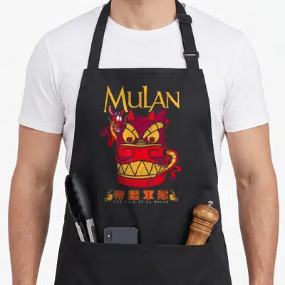 Tablier de cuisine noir avec illustration colorée de Mushu et d'un masque rouge stylisé aux yeux jaunes.