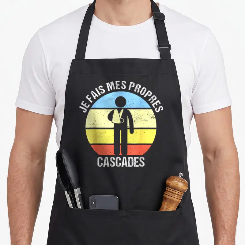Tablier de cuisine noir avec une silhouette en écharpe et le texte Je Fais Mes Propres Cascades sur un cercle multicolore.