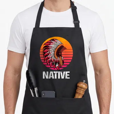Tablier de cuisine noir avec illustration de plumage amérindien sur fond circulaire orange et rose et le mot NATIVE en bas.