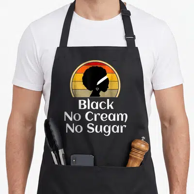 Tablier de cuisine noir avec silhouette femme afro et texte Black No Cream No Sugar sur fond dégradé vintage.
