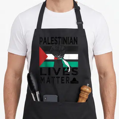 Tablier de cuisine noir avec un poing levé, le drapeau palestinien et l'inscription Palestinian Lives Matter accompagnée d'une silhouette de mosquée.