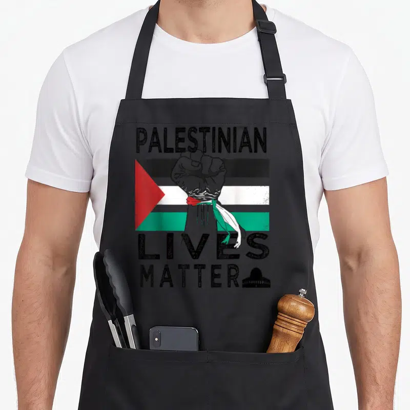 Tablier de cuisine noir avec un poing levé, le drapeau palestinien et l'inscription Palestinian Lives Matter accompagnée d'une silhouette de mosquée.
