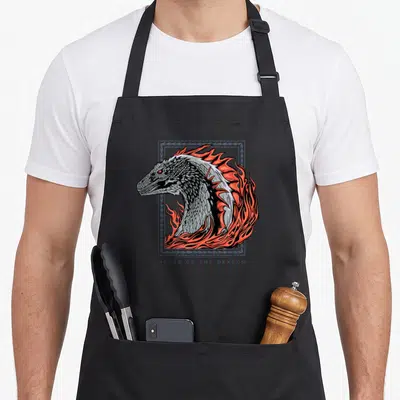 Tablier de cuisine noir avec tête de dragon grise entourée de flammes oranges et cadre décoratif bleu-gris.