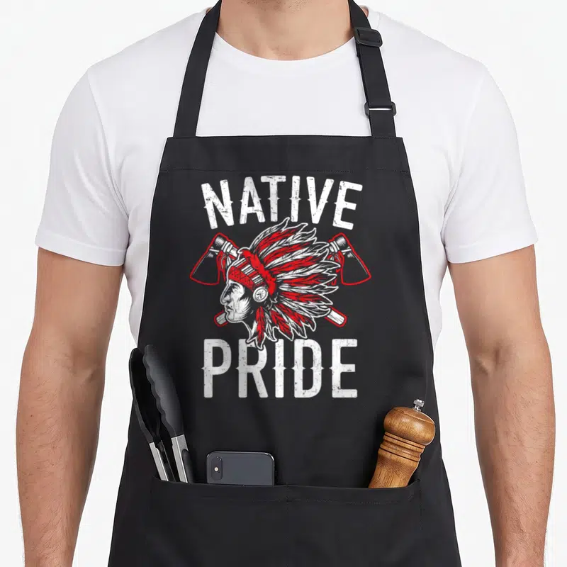 Tablier de cuisine noir avec illustration coiffe amérindienne haches croisées texte Native Pride blanc et rouge.