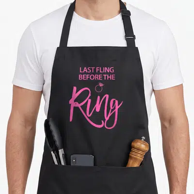 Tablier de cuisine noir avec inscription rose Dernière Aventure Avant La Bague et icône d'alliance.