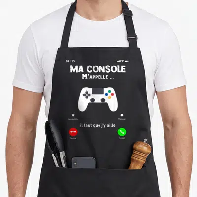 Tablier de cuisine noir avec motif simulateur d'appel téléphonique et manette de jeu vidéo blanche au centre.