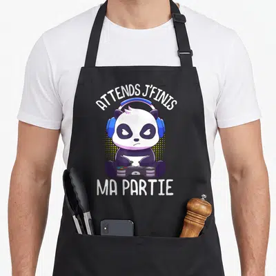 Tablier de cuisine noir avec un panda gamer aux écouteurs bleus tenant une manette et le texte Attends j'finis ma partie.