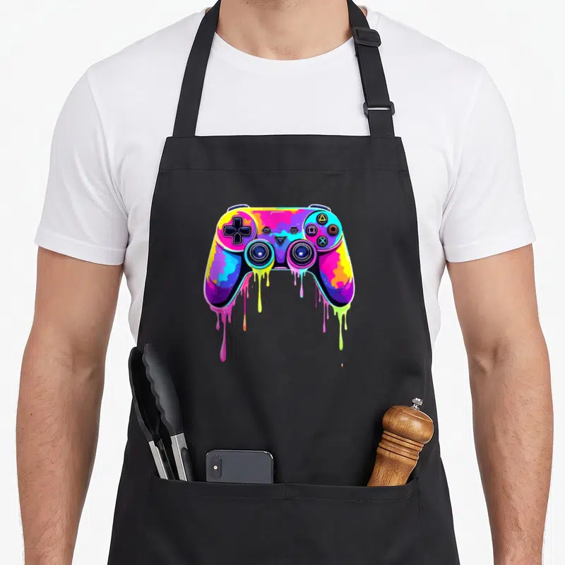 Tablier de cuisine noir avec une illustration de manette de jeu vidéo multicolore aux couleurs qui dégoulinent.