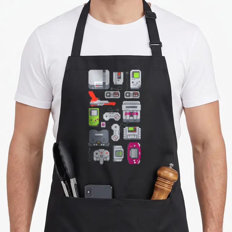Tablier de cuisine noir avec consoles, manettes et machines à sous en pixel art colorées disposées verticalement.