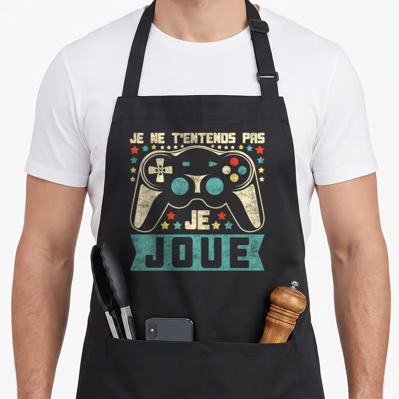 Tablier de cuisine noir avec une manette de jeu vidéo vintage et des étoiles colorées.