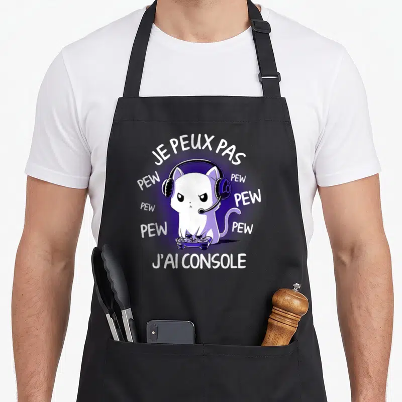 Tablier de cuisine noir avec un chat blanc en train de jouer à la console sous un halo violet.