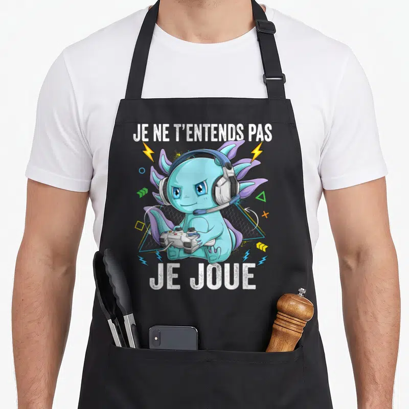 Tablier de cuisine noir avec un axolotl bleu gamer portant des écouteurs et tenant une manette de jeu vidéo.