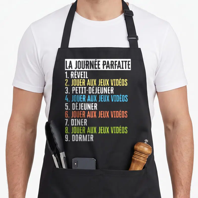 Tablier de cuisine noir avec une liste colorée intitulée La Journée Parfaite listant jouer aux jeux vidéos à plusieurs reprises.