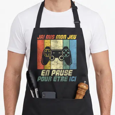 Tablier de cuisine noir avec manette de console colorée et texte J'ai mis mon jeu en pause pour être ici.