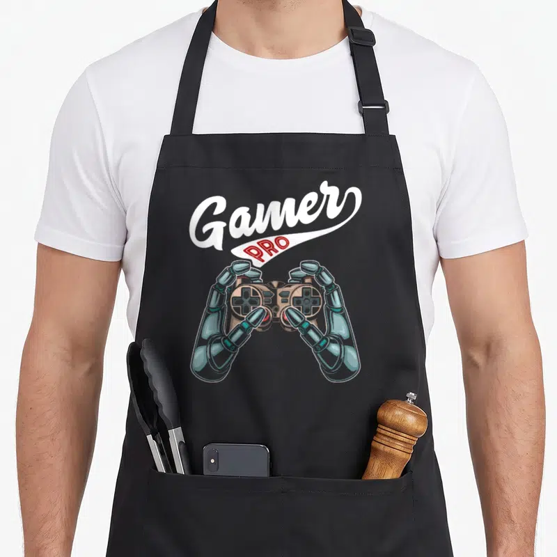 Tablier de cuisine noir avec des mains robotiques tenant une manette et le texte Gamer Pro
