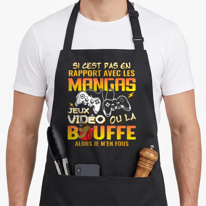 Tablier de cuisine noir avec texte jaune et orange sur les mangas, jeux vidéos et bouffe, illustré par deux manettes et un carton de noodles.