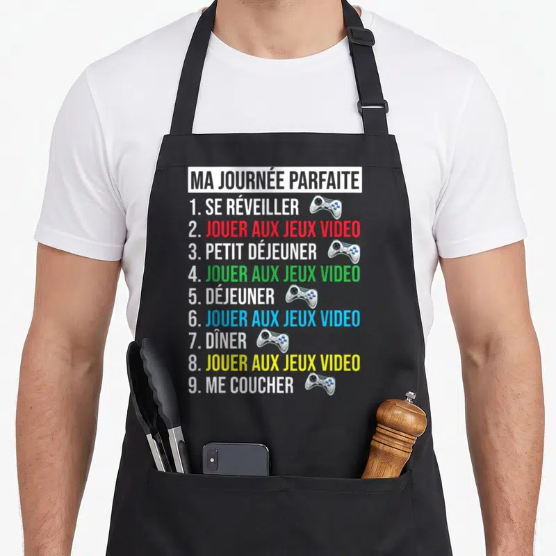 Tablier de cuisine noir avec liste humoristique Ma Journée Parfaite et illustrations de manettes de jeu colorées.