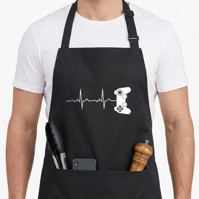 Tablier de cuisine noir avec une ligne de vie blanche se terminant par une manette de jeu vidéo.