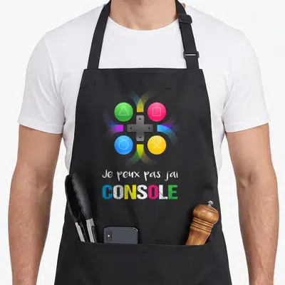 Tablier de cuisine noir avec pad de jeu coloré et texte Je peux pas j'ai CONSOLE imprimé en blanc et multicolore.