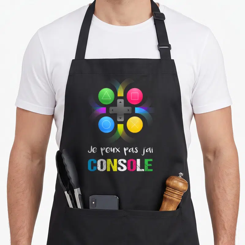 Tablier de cuisine noir avec pad de jeu coloré et texte Je peux pas j'ai CONSOLE imprimé en blanc et multicolore.