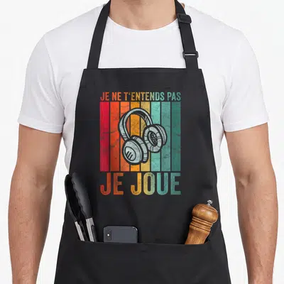 Tablier de cuisine noir avec illustration d'écouteurs sur fond de bandes colorées verticales et texte humoristique gaming.