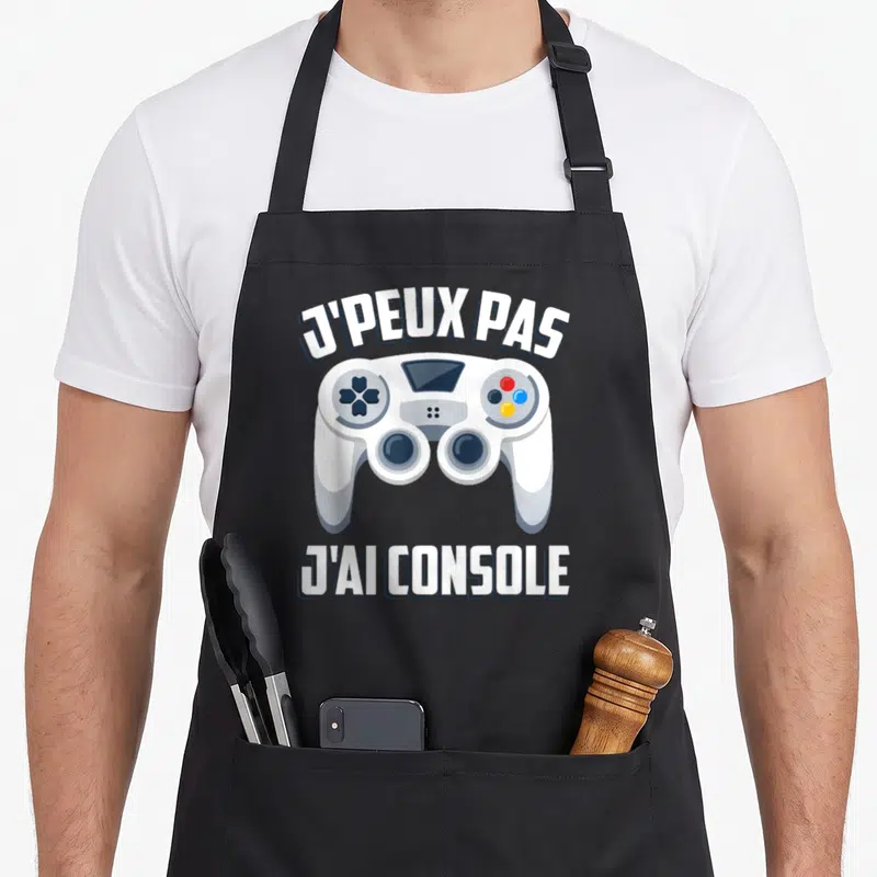 Tablier de cuisine noir avec illustration manette blanche et texte J'peux pas j'ai console