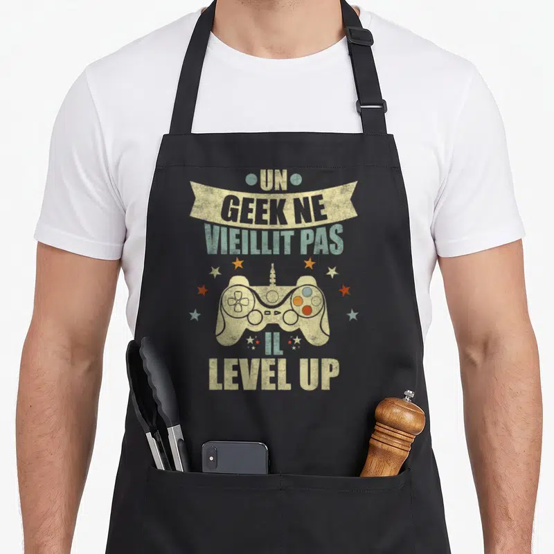 Tablier de cuisine noir avec manette de jeu vidéo et texte Un geek ne vieillit pas il level up