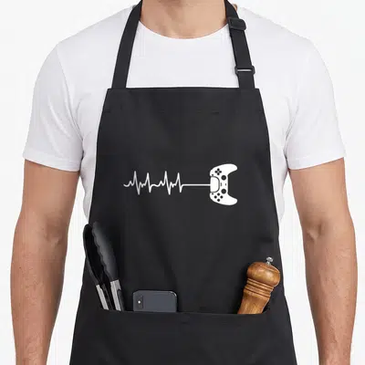 Tablier de cuisine noir avec une illustration blanche représentant une manette de jeu dont le fil devient une courbe cardiaque.