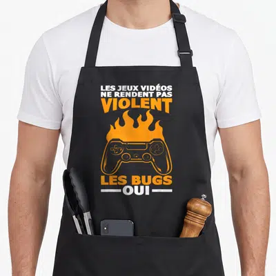 Tablier de cuisine noir avec une console orange enflammée et le texte Les jeux vidéos ne rendent pas violent les bugs oui.