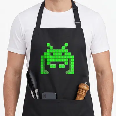 Tablier de cuisine noir avec un alien pixelisé vert style arcade 8 bits géométrique.