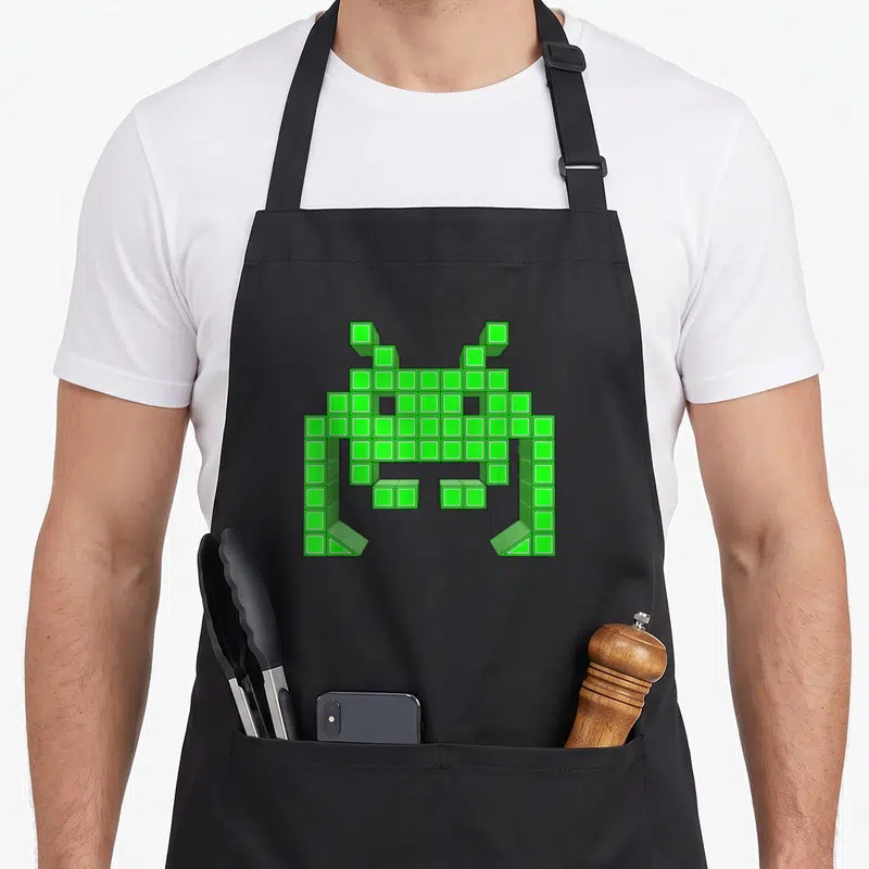 Tablier de cuisine noir avec un alien pixelisé vert style arcade 8 bits géométrique.