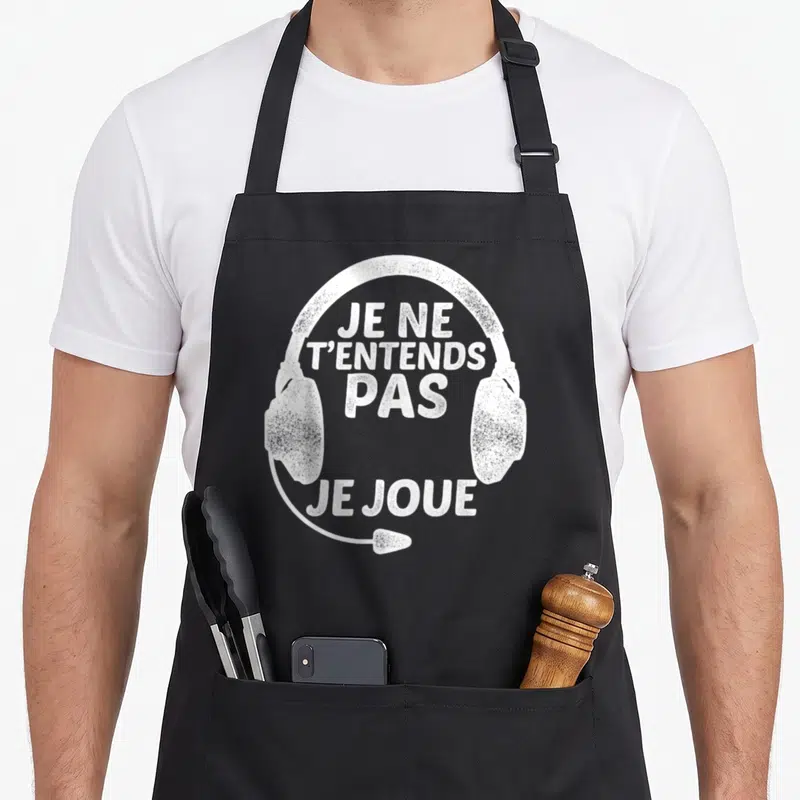 Tablier de cuisine noir avec illustration blanche d'un casque audio et le texte Je ne t'entends pas je joue au centre.